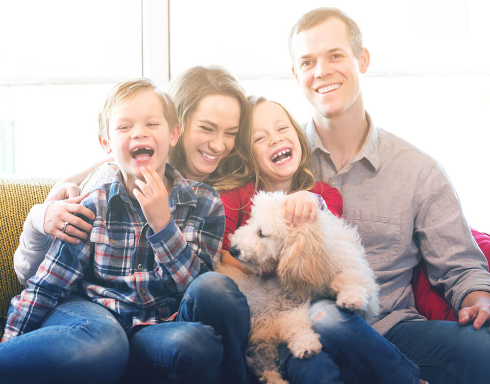 A laughing family on the couch with their dog.